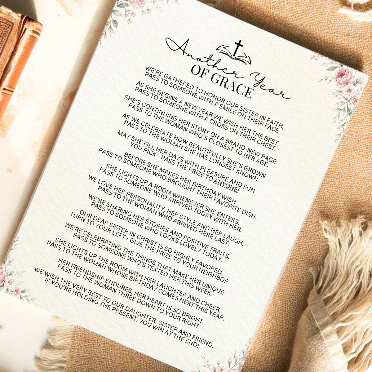 A printed 'Another Year of Grace' birthday message card with a floral design, styled on a rustic beige fabric background next to a wooden spoon.