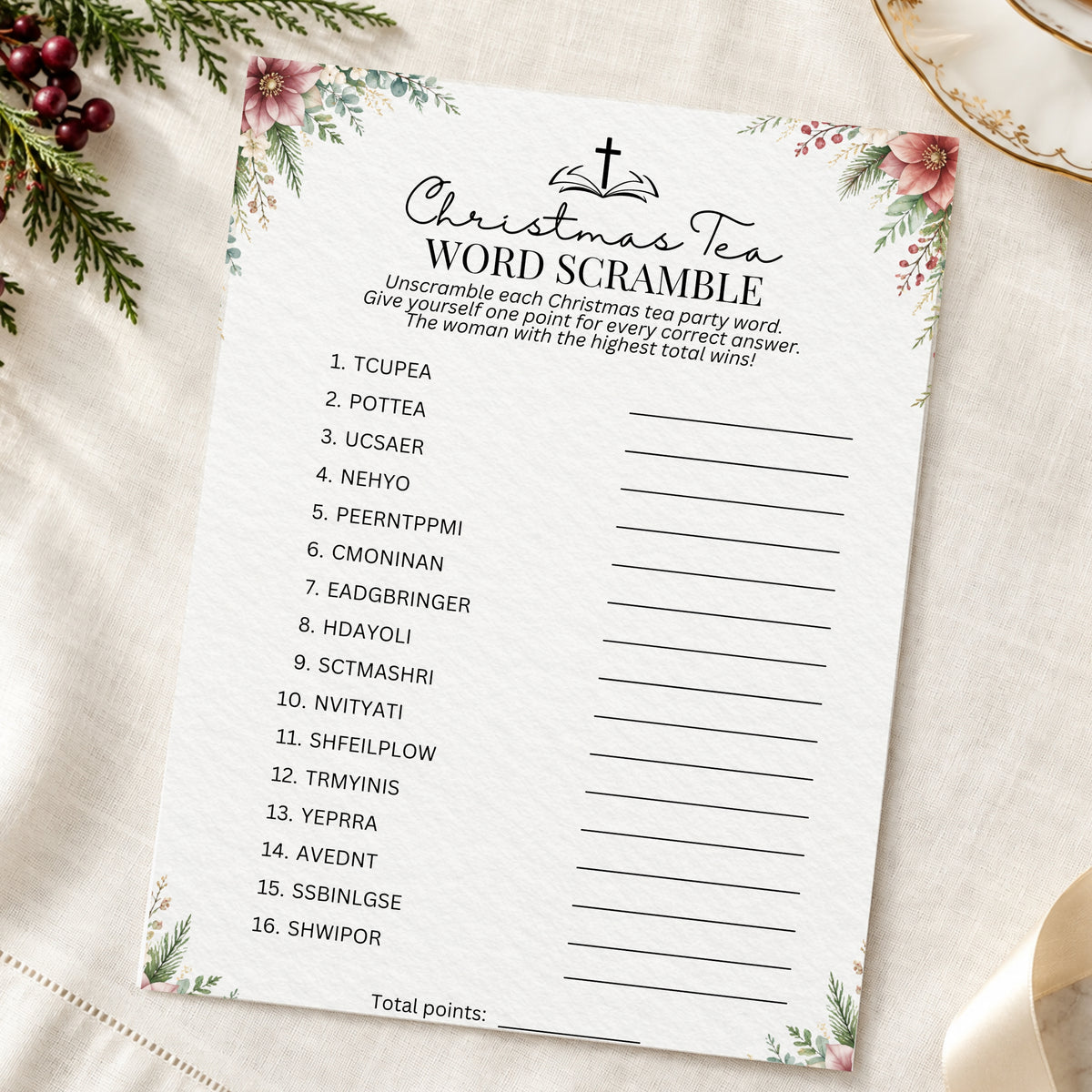 A Christmas-themed word scramble printable game card laid flat on a textured cream fabric with floral borders, green pine branches, and a gold plate edge visible around it.